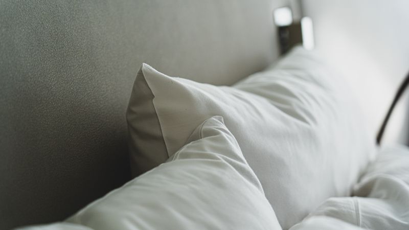 Cama arrumada com lençóis e travesseiros brancos em um quarto claro e aconchegante