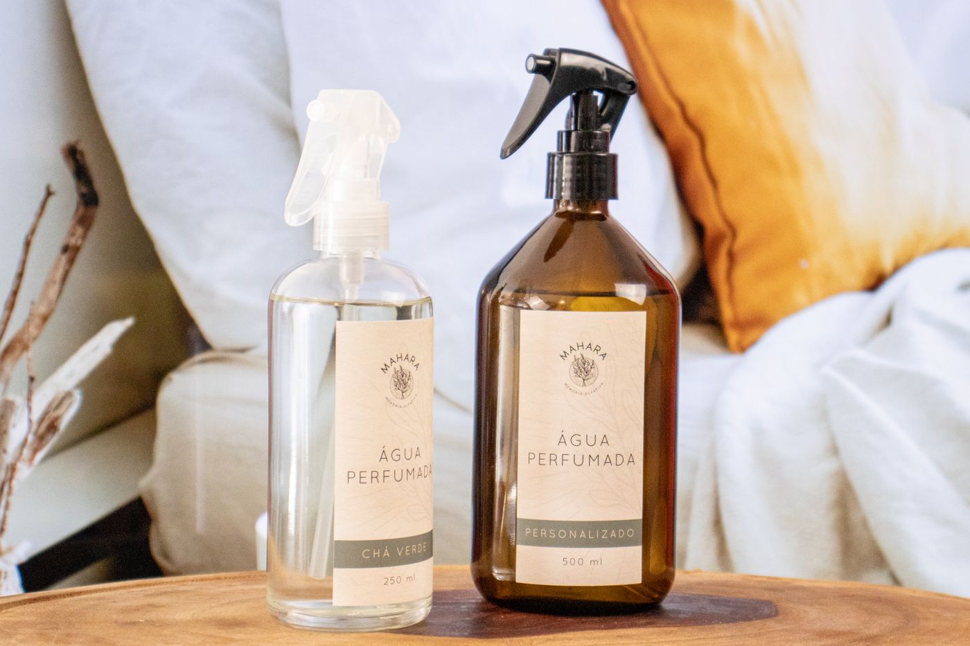 Dois frascos de água aromática com válvula spray, um de vidro âmbar e um de vidro transparente, sobre uma mesa de madeira